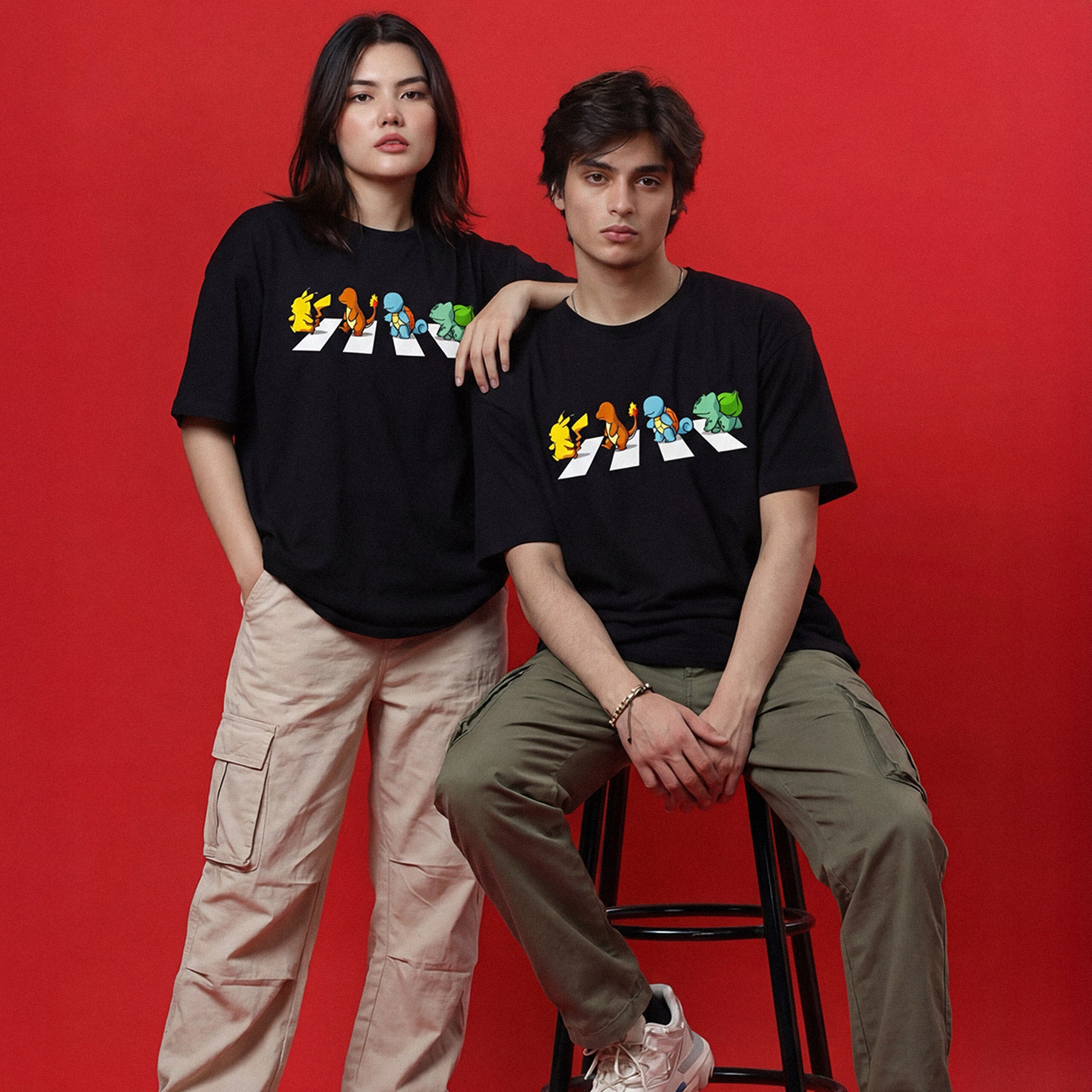 Two people wearing black t-shirts with colorful graphic designs on a red background